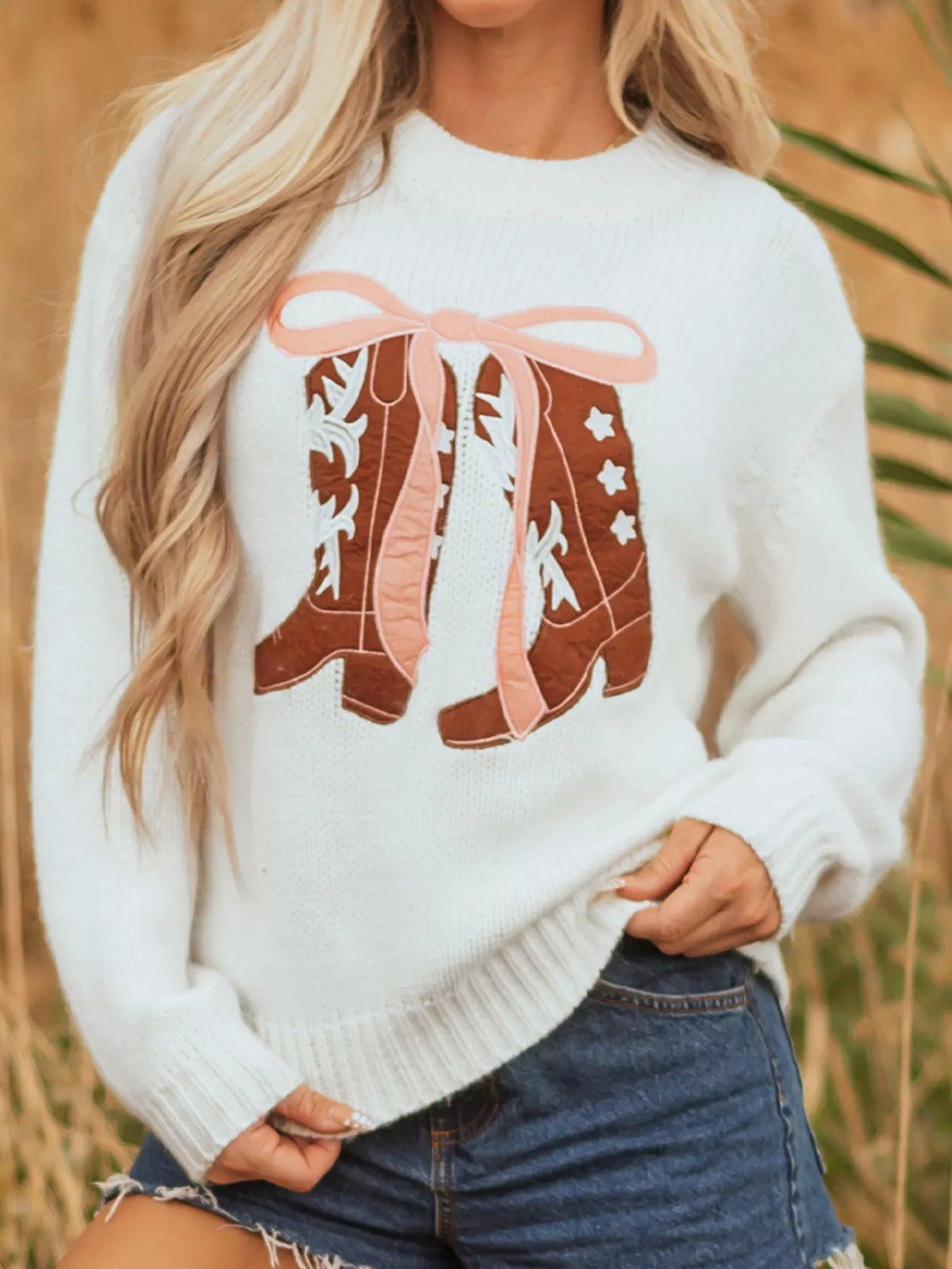 Women's Embroidered Bow Boots Drop Shoulder Sweater in cream, laid flat showing the detailed boot and bow design on the front.