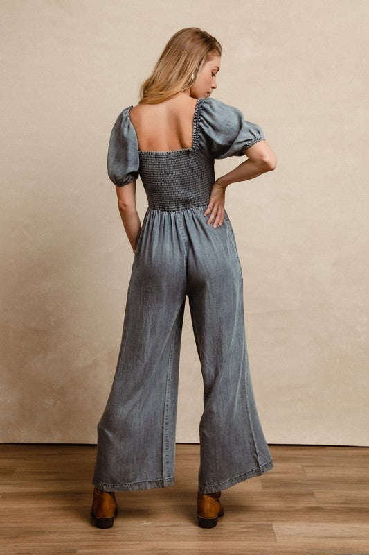 BiBi Smocked Denim Jumpsuit with square neck and puff sleeves on model