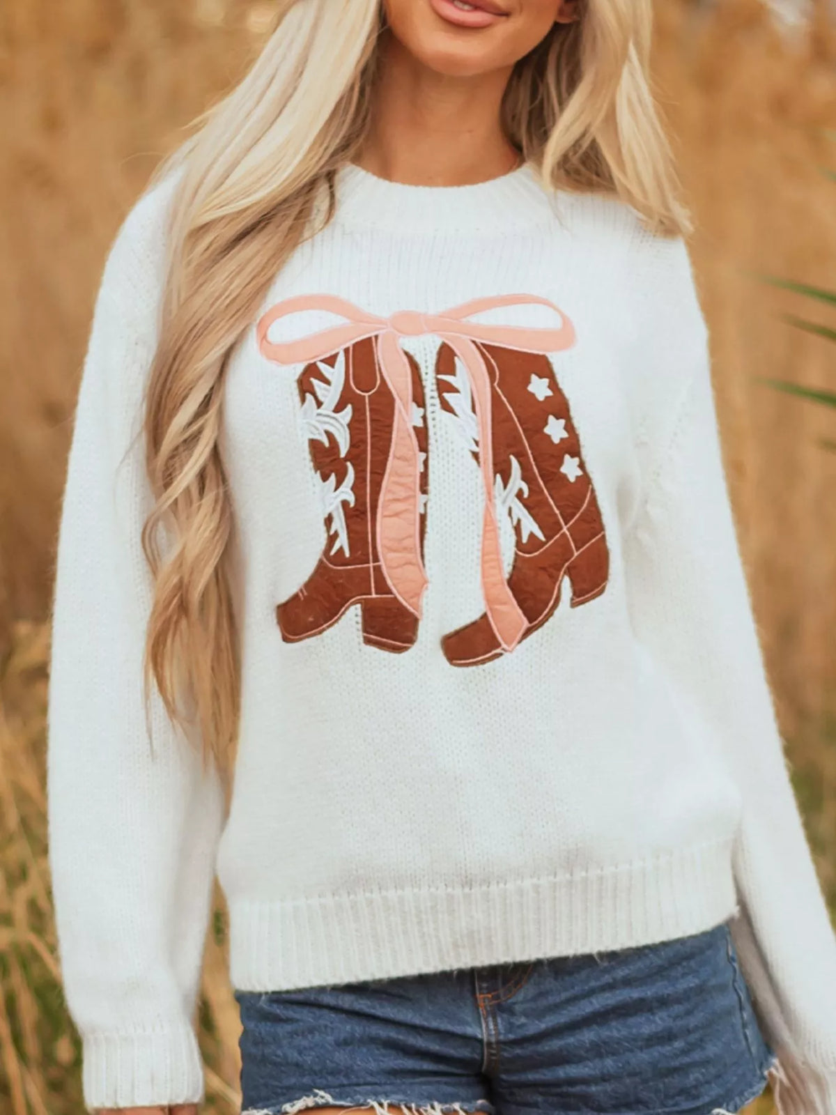 Women's Embroidered Bow Boots Drop Shoulder Sweater in cream, laid flat showing the detailed boot and bow design on the front.